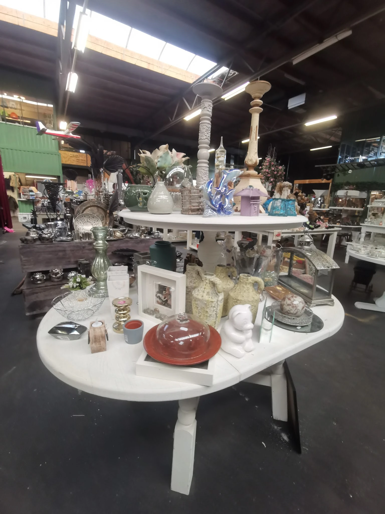 Witte ronde tafels met decoratieve huishoudartikelen: vazen, kaarsenhouders, schalen en verschillende keramische en glazen ob