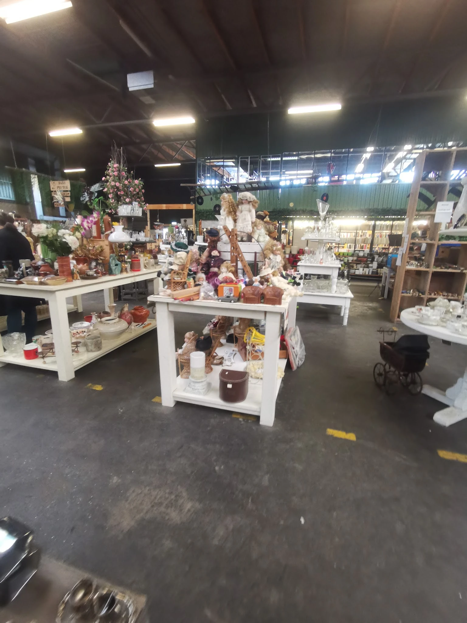 Winkelvloer met witte display-tafels vol met decoratieve items, kaarsen en huishoudspullen in een kringloopwinkel