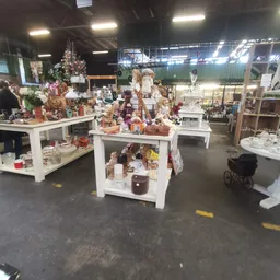 Winkelvloer met witte display-tafels vol met decoratieve items, kaarsen en huishoudspullen in een kringloopwinkel