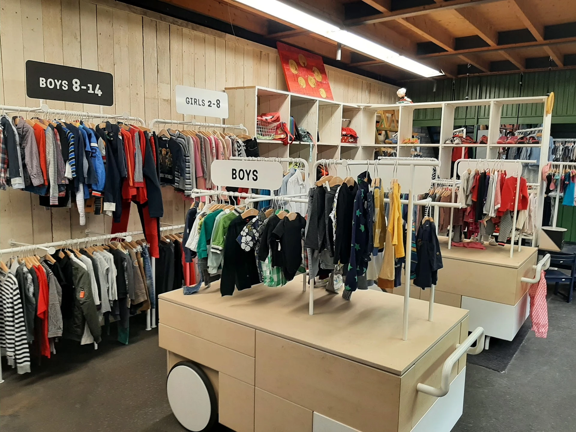 Kringloopwinkelafdeling met kinderkleding, stellingen en een centrale display met jongens- en meisjeskleding