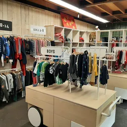 Kringloopwinkelafdeling met kinderkleding, stellingen en een centrale display met jongens- en meisjeskleding