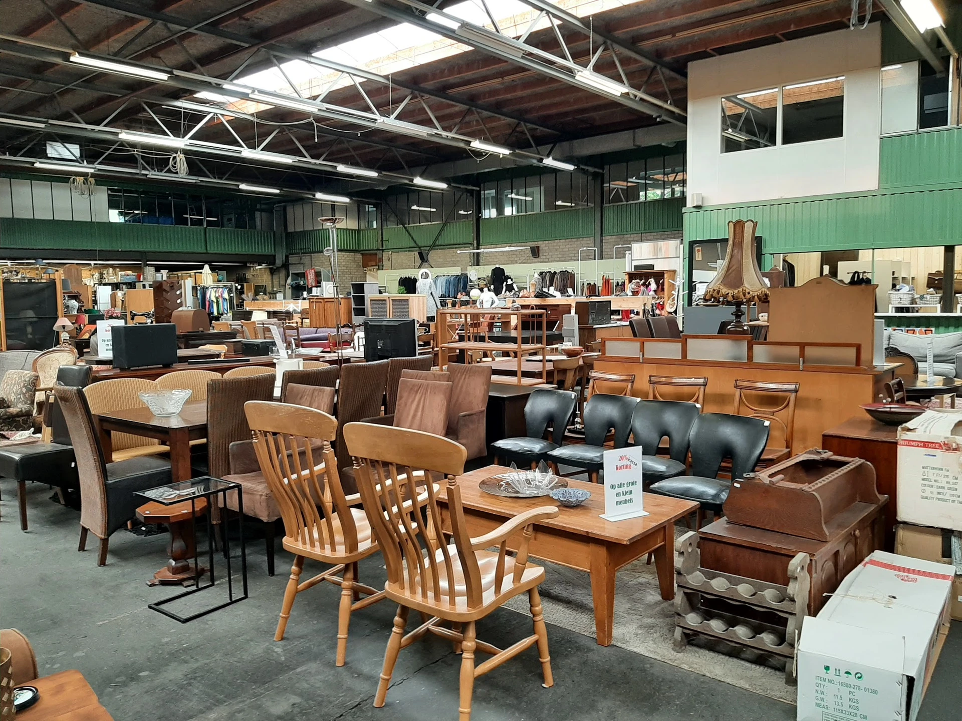 Winkelvloer met diverse meubelen: houten stoelen, tafels, bruine leren banken en kasten onder industrieel plafond