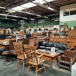 Winkelvloer met diverse meubelen: houten stoelen, tafels, bruine leren banken en kasten onder industrieel plafond