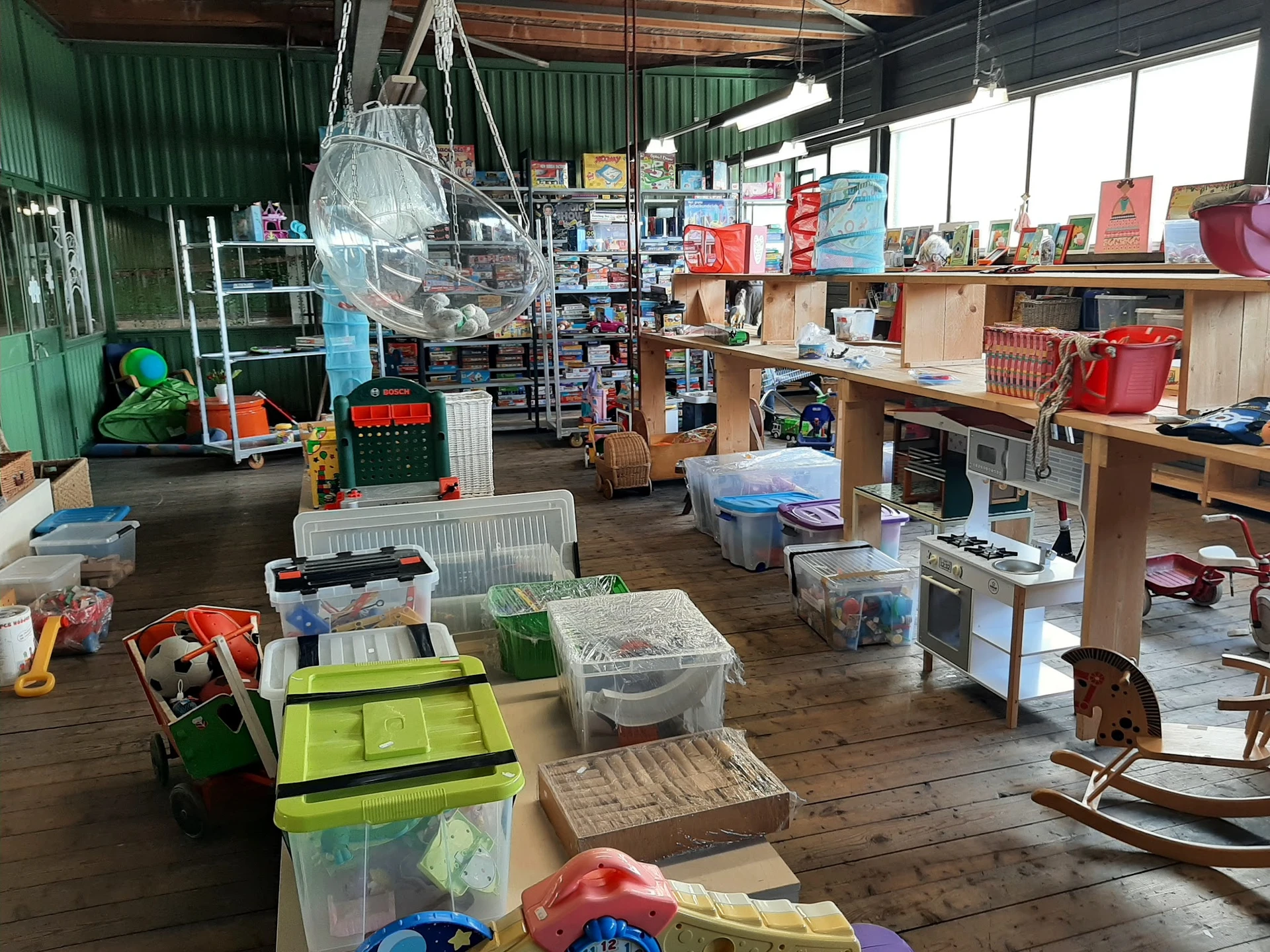 Ruim winkelinterieur met diverse artikelen, stellingen, dozen en spullen verspreid over houten vloer