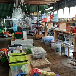 Ruim winkelinterieur met diverse artikelen, stellingen, dozen en spullen verspreid over houten vloer