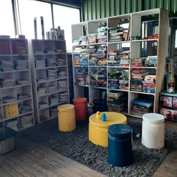 Winkelvloer met stellingen vol dvd's, boeken en spullen, enkele zitpoefjes en grijze vloerkleed