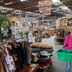 Overzicht van kringloopwinkelhal met kledingrekken, meubels, huishoudspullen en decoratiestukken.
