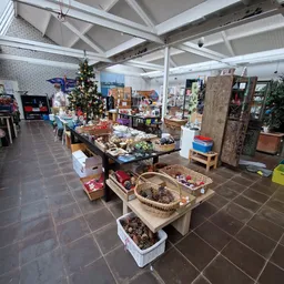 Overzicht van kringloopwinkel met tafels vol gebruiksartikelen, decoraties en spullen, hoog plafond met raamwerk