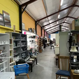 Binnenaanzicht van kringloopwinkel met stellingen, vitrines en diverse tweedehands artikelen langs de winkelvloer