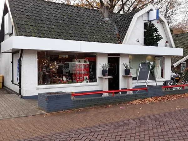 Witte kringloopwinkel met donker pannendak, grote etalageruit met rood accent, bakstenen voorgevel aan straat