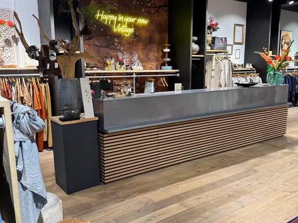 Winkelvloer met brede toonbank met houten latten, rekken met kleding, decoratie en gele neonbord op achtergrond