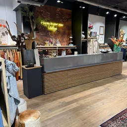 Winkelvloer met brede toonbank met houten latten, rekken met kleding, decoratie en gele neonbord op achtergrond