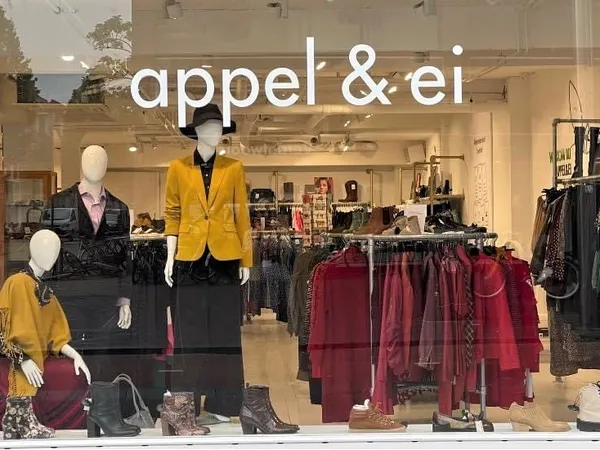 Winkelinterieur met etalagepoppen in kleding, kledingrekken en uitgestalde artikelen in rode en gele tinten