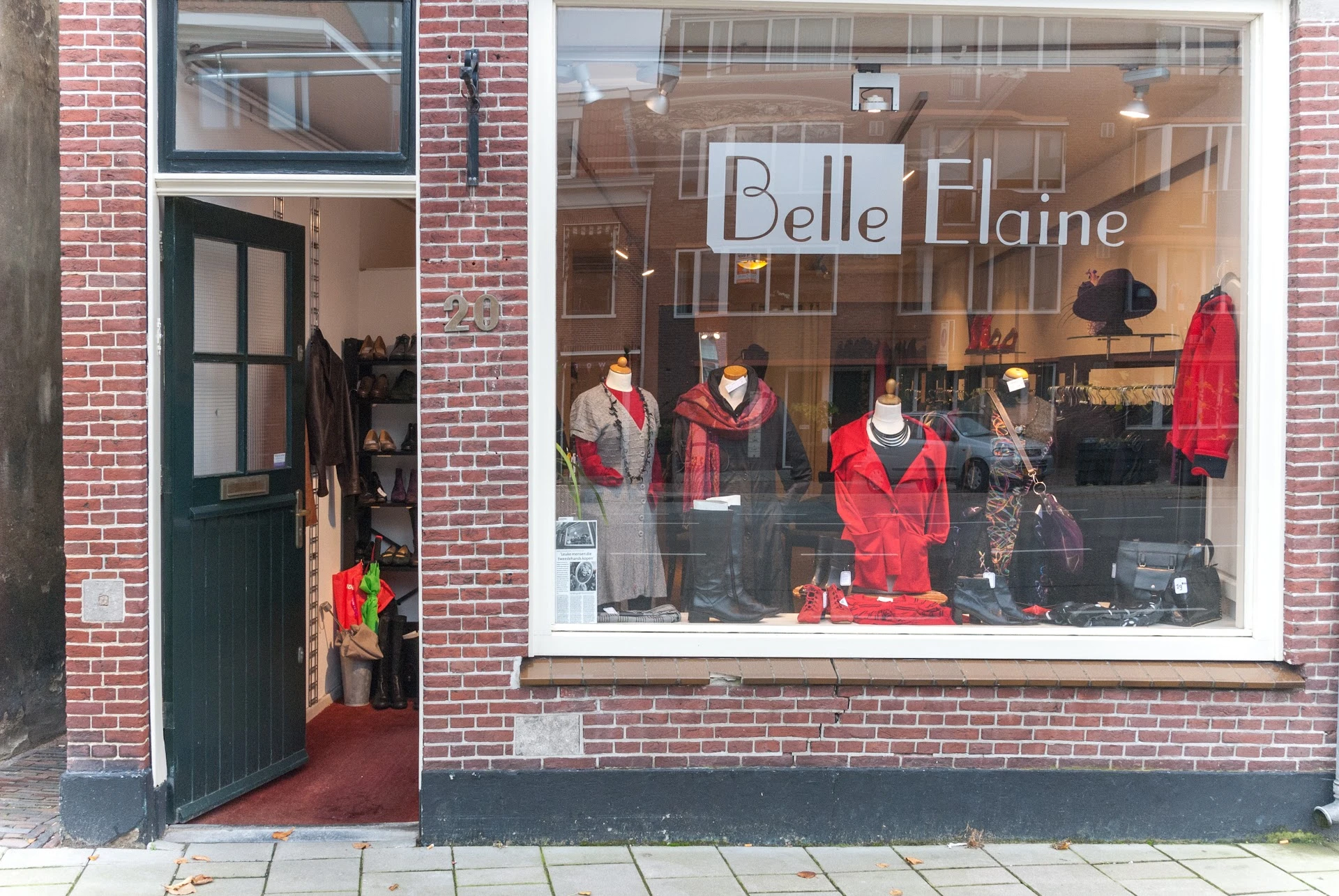 Winkelfront met rode deur, groot etalageraam met kledingmanequins in rode en grijze kleding, en 'Belle Elaine' tekst op het r