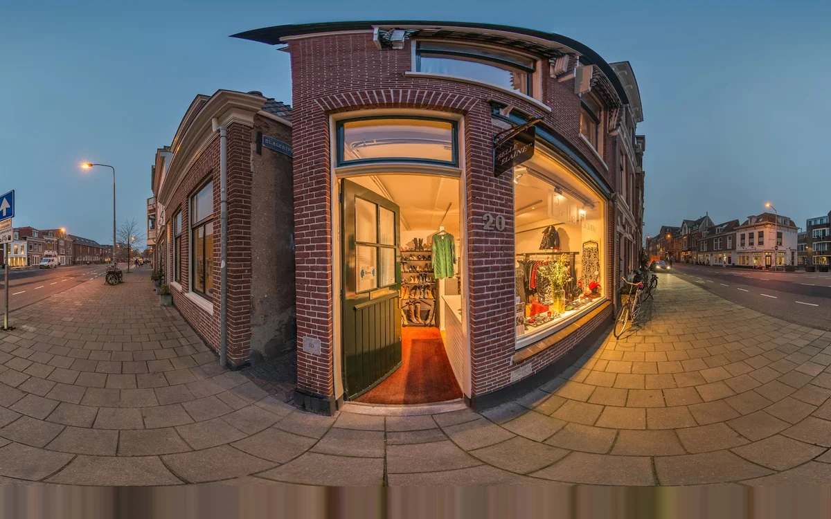 Hoekpand met rode bakstenen gevel en grote verlichte etalages, winkelinterieur zichtbaar door ramen