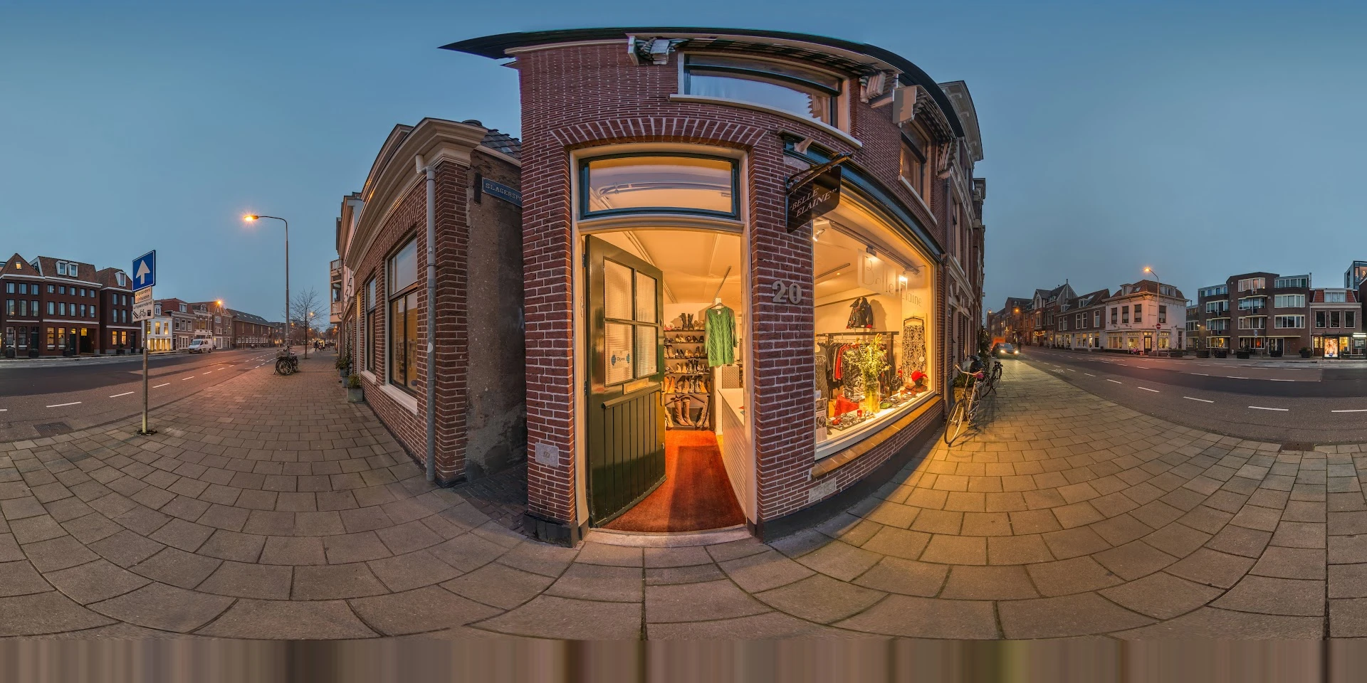 Hoekpand met rode bakstenen gevel en grote verlichte etalages, winkelinterieur zichtbaar door ramen