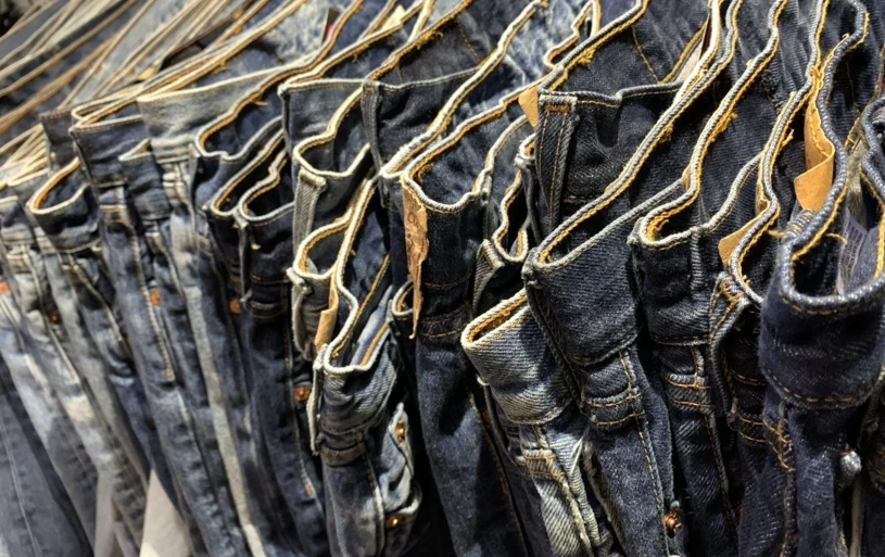 Rekken met tweedehands jeans, opgehangen aan gouden hangers, verschillende wassingen en kleuren