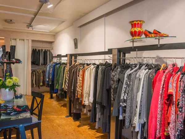 Winkelvloer met rekken vol tweedehands kleding, oranje vloer en witte wanden