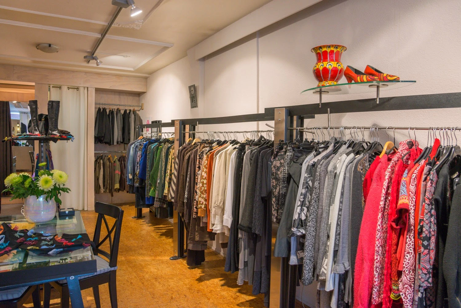 Winkelvloer met kledingrekken vol tweedehands kleding in verschillende kleuren, oranje vloer en witte plafondverlichting