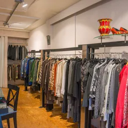 Winkelvloer met kledingrekken vol tweedehands kleding in verschillende kleuren, oranje vloer en witte plafondverlichting