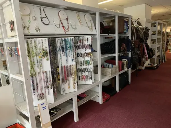 Winkelinterieur met witte stellingen vol sieraden, kettingen en armbanden in verschillende kleuren, en daarachter rekken met 