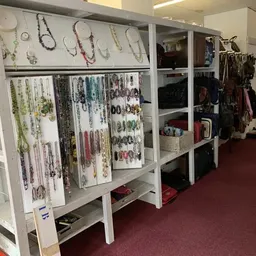 Winkelvloer met witte stellingen vol sieraden, kettingen en accessoires, op de achtergrond kleding aan rekken