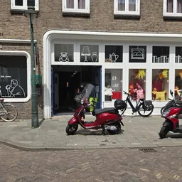 Winkelgevel met witte uitstalkast, zwartbord links, fietsen en scooters op het terras ervoor