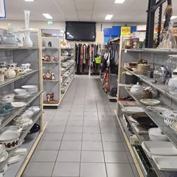 Winkelinterieur met glazen vitrines met servies en huishoudwaar aan beide zijden, kleding aan hangers in het midden, schoon e