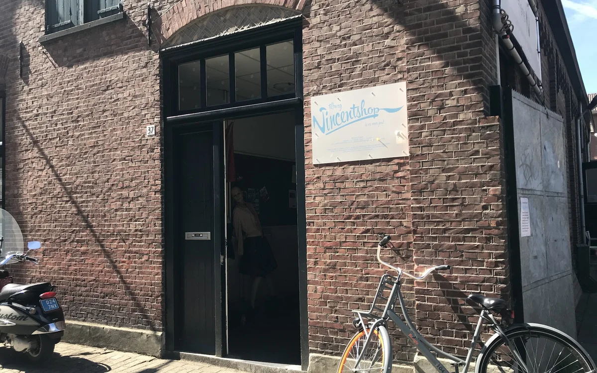 Bakstenen gevel van kringloopwinkel met zwarte deur en raam, fietsen geparkeerd ervoor