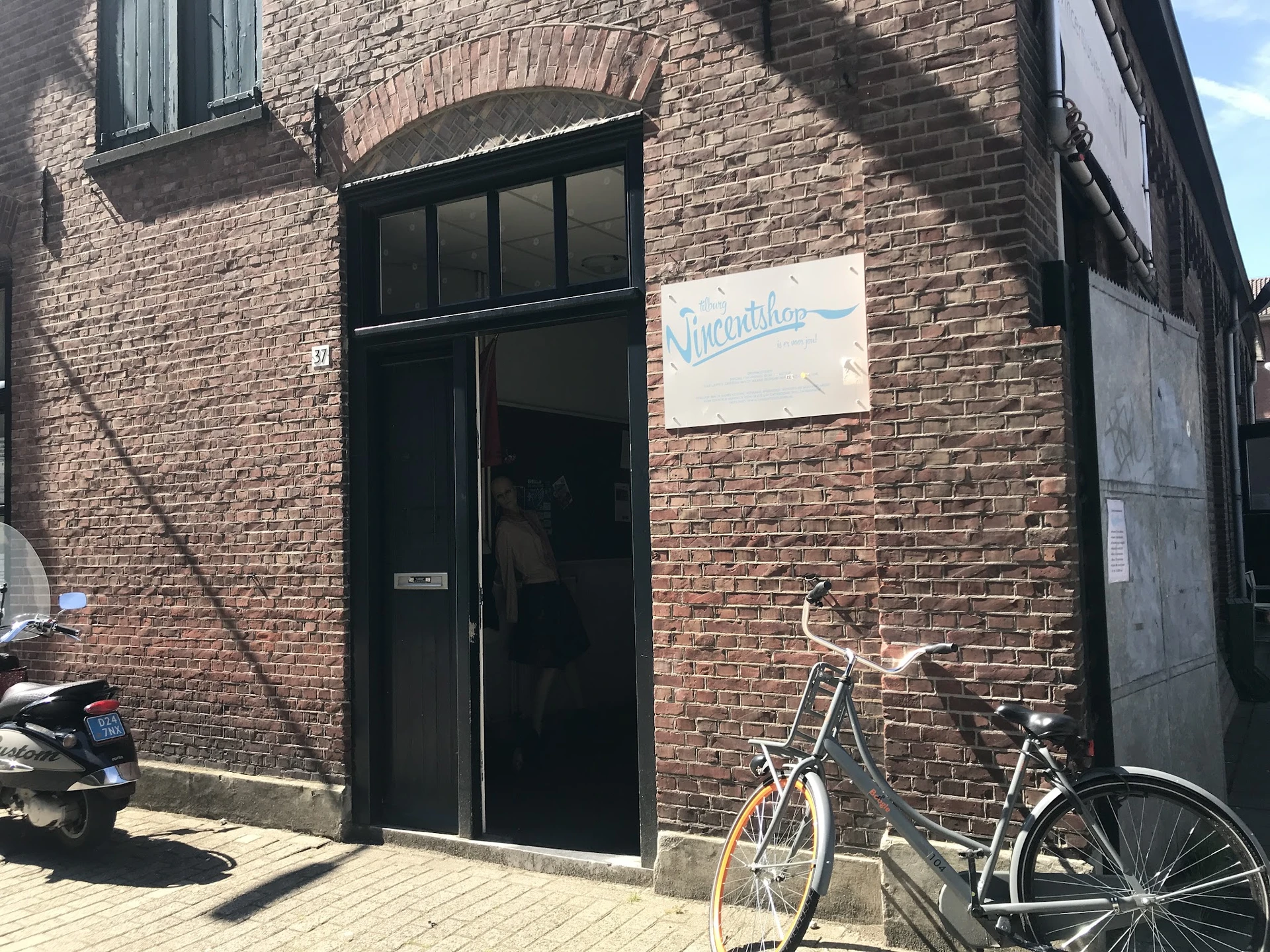 Bakstenen gevel van kringloopwinkel met zwarte deur en raam, fietsen geparkeerd ervoor