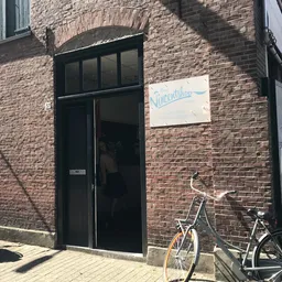 Bakstenen gevel van kringloopwinkel met zwarte deur en raam, fietsen geparkeerd ervoor