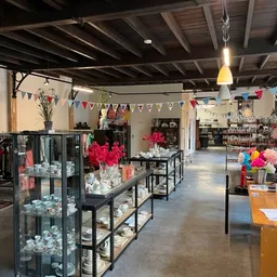 Ruim kringloopwinkelinterieur met kledingrekken links, glazen vitrines in het midden met decoratieve items, en diverse goeder