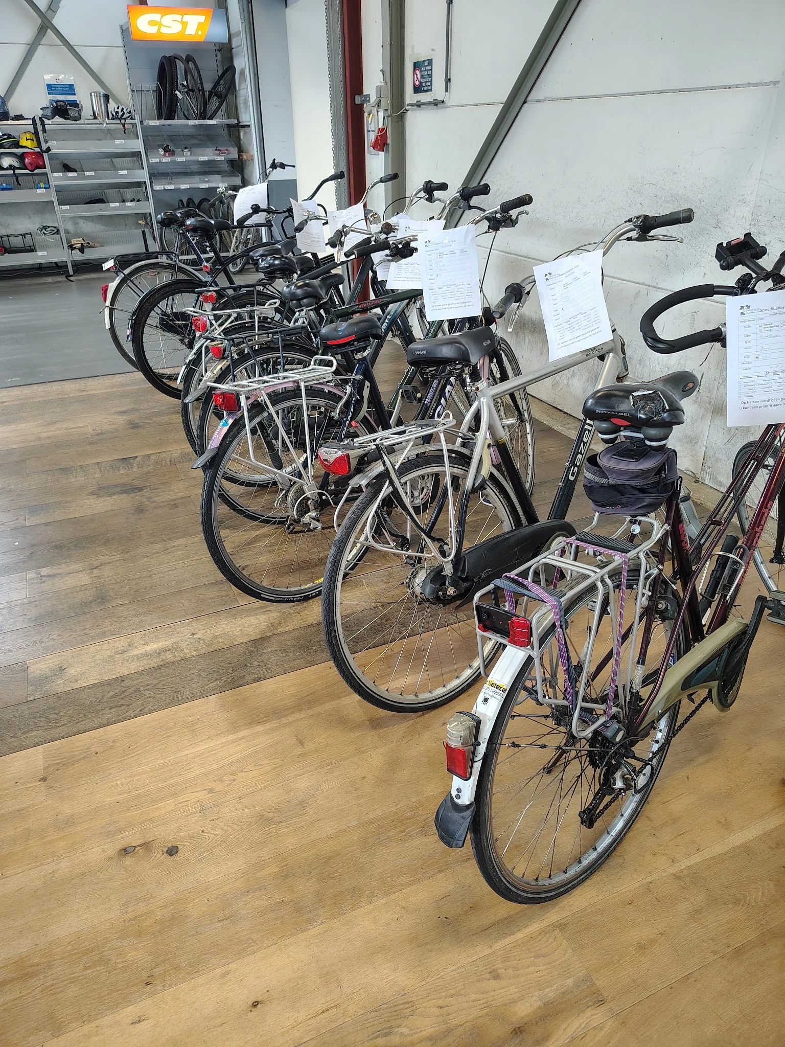 Rij tweedehands fietsen met rode reflectoren en zwarte zadels uitgestald in de winkel