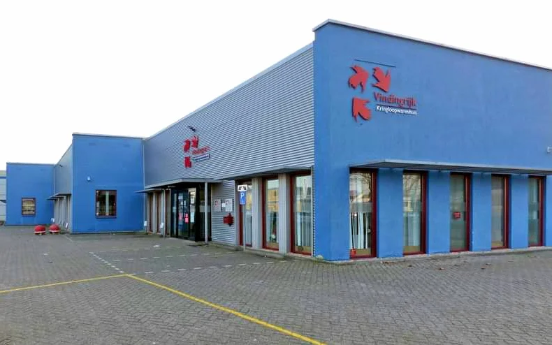 Blauwe gevel van kringloopwarenhuis Vindingrijk met rode letters, ingangsdeuren en ramen