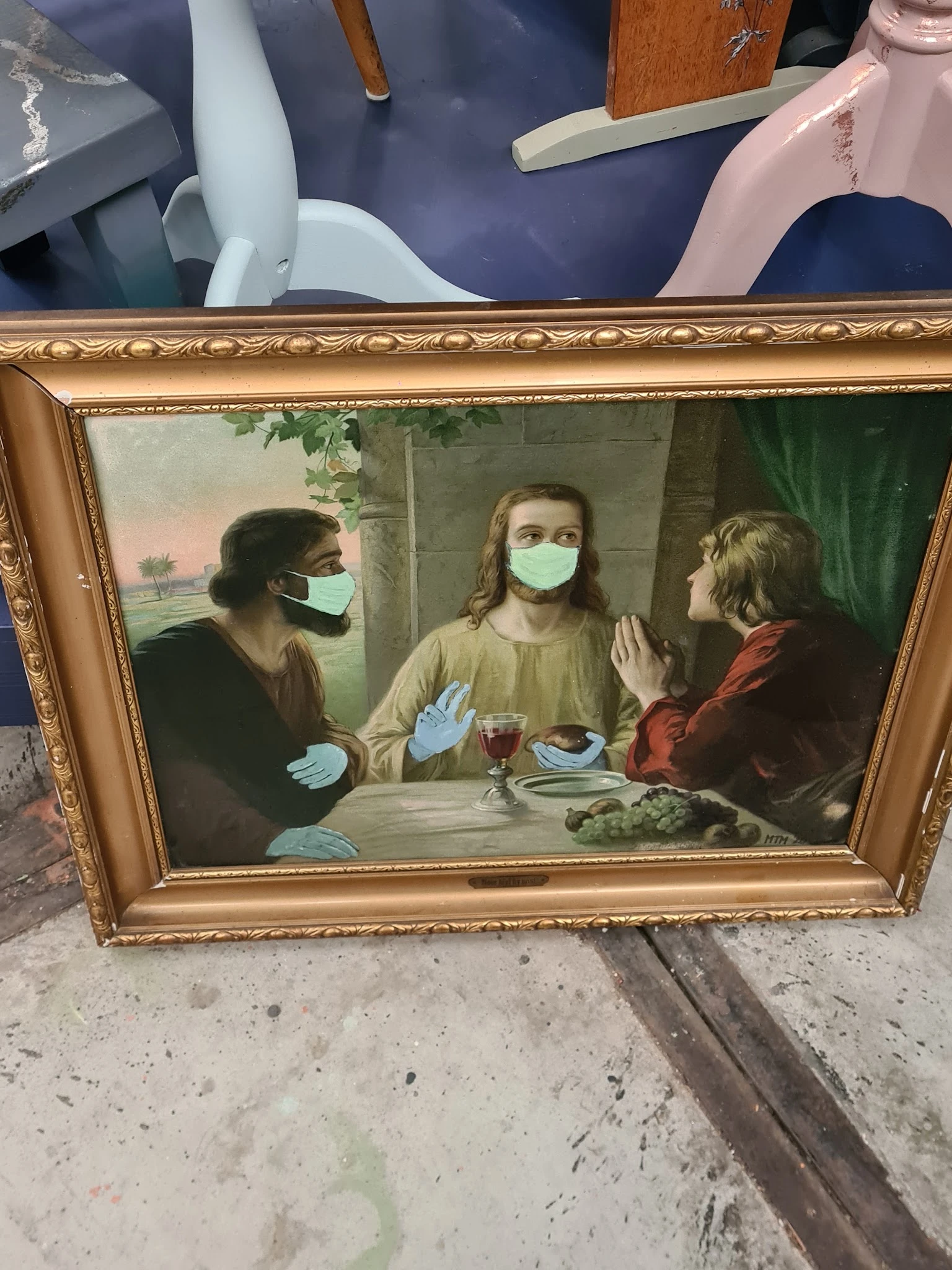 Goudkleurig ingelijst schilderij met drie figuren in medische maskers rond een tafel
