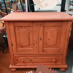 Oranje vintage kastje met twee deuren en een lade, met versleten afwerklaag