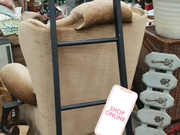 Beige fauteuil met zwart frame en houten armleuningen naast serviesgoed en andere meubels in de winkel