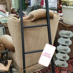 Beige fauteuil met zwart frame en houten armleuningen naast serviesgoed en andere meubels in de winkel