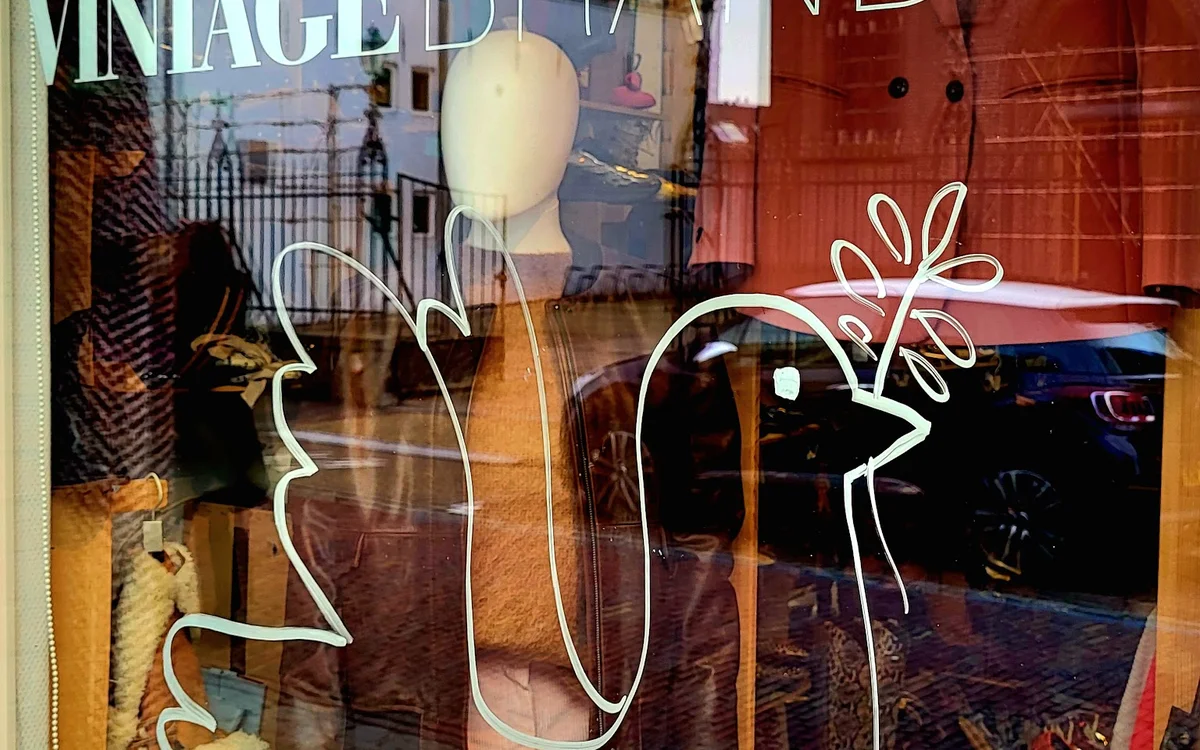 Etalageruit met winkelmanequin en decoratieve tekening, reflecties van straat zichtbaar