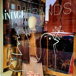 Etalageruit met winkelmanequin en decoratieve tekening, reflecties van straat zichtbaar