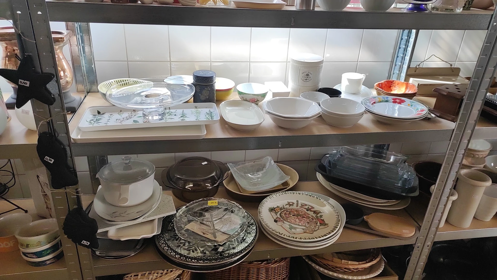 Schappen met servies en borden, waaronder witte kommen, decoratieve borden en aardewerk uit de tweedehandswinkel