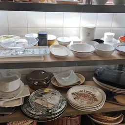 Schappen met servies en borden, waaronder witte kommen, decoratieve borden en aardewerk uit de tweedehandswinkel
