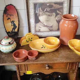 Uitgestalde vintage serviesgoed op houten tafel: gele en oranje keramische schalen, rode potjes en decoratieve items