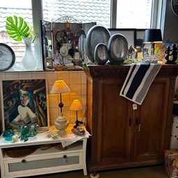 Vitrinekast met vintage lampen, kunstwerk, glazen en decoratieve items in een kringloopwinkel