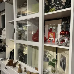 Vitrinekast met kerstdecoratie en huishoudelijke artikelen, waaronder rode kerstballen, een sneeuwbol en diverse decorstukken