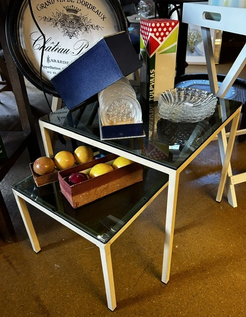 Vintage meubels en huishoudspullen uitgestald op tafels: glazen schalen, kristal, gele bollen en een houten bakje met spullen