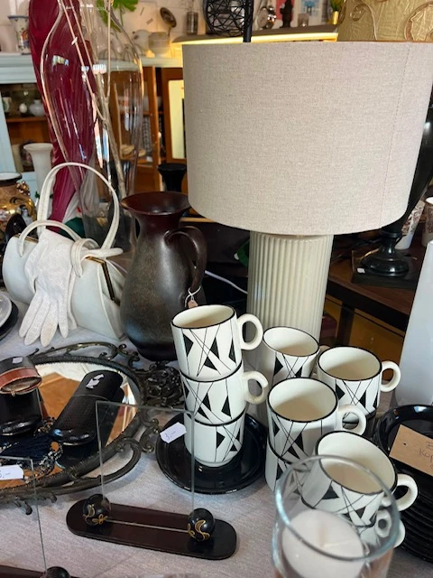 Uitgestalde servies en huishoudartikelen, waaronder kopjes met geometrisch patroon en een theepot