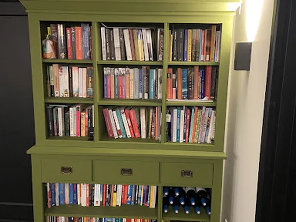 Groengeverfde boekenkast met negen vakken vol dvd's en cd's, onderste compartimenten met flessen wijn
