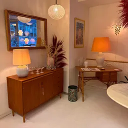 Vintage woonkamervignette met houten dressoir, lamp, tv-frame aan muur, bloemstuk en houten bijzettafel met lamp