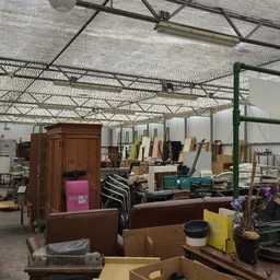 Binnenaanzicht van kringloopwinkel met houten meubels, stellingen en diverse tweedehandsartikelen onder aluminium ligger-cons